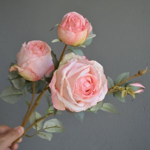 May include: A bouquet of four pink artificial roses with green leaves. The roses are in various stages of bloom, with one fully open and the others in bud form.