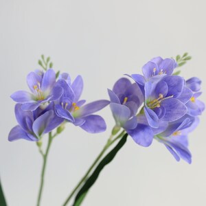 Puede incluir: Un ramo de flores de lavanda artificiales con tallos verdes. Las flores son de color lila claro con centros amarillos.