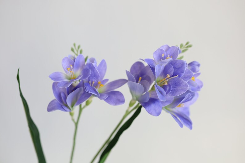 Puede incluir: Un ramo de flores de lavanda artificiales con tallos verdes. Las flores son de color lila claro con centros amarillos.