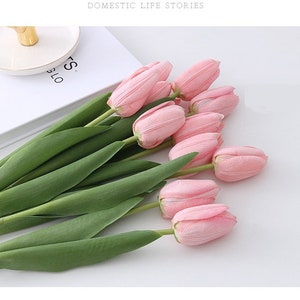 May include: A bouquet of pink artificial tulips with green stems. The tulips are arranged in a loose, natural-looking way.