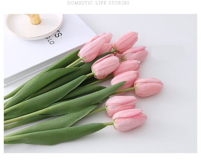 May include: A bouquet of pink artificial tulips with green stems. The tulips are arranged in a loose, natural-looking way.