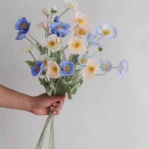 Puede incluir: Un ramo de flores artificiales con flores de amapola de color azul, blanco y melocot&oacute;n. Los tallos son verdes y tienen una textura peluda.