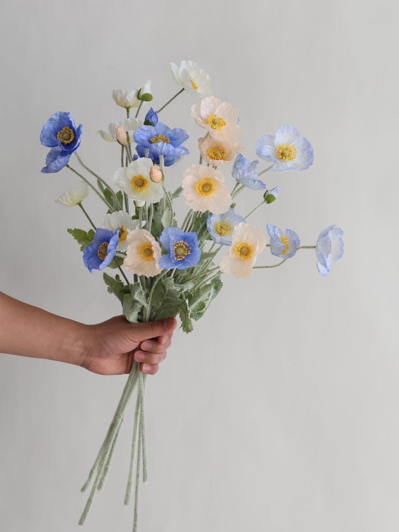 Puede incluir: Un ramo de flores artificiales con flores de amapola de color azul, blanco y melocot&oacute;n. Los tallos son verdes y tienen una textura peluda.