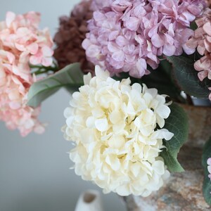Puede incluir: Un ramo de hortensias artificiales en una variedad de colores, incluyendo rosa, blanco y morado. Las flores est&aacute;n dispuestas en un jarr&oacute;n y son una hermosa adici&oacute;n a cualquier decoraci&oacute;n del hogar.