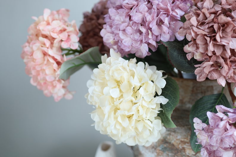 Puede incluir: Un ramo de hortensias artificiales en una variedad de colores, incluyendo rosa, blanco y morado. Las flores est&aacute;n dispuestas en un jarr&oacute;n y son una hermosa adici&oacute;n a cualquier decoraci&oacute;n del hogar.