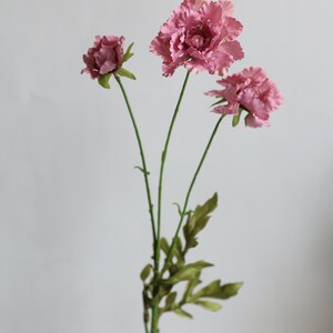 May include: A stem of artificial flowers featuring three dusty rose-colored blooms with ruffled petals and green leaves on a thin stalk. The text "Red Bean" is printed in black in the bottom right corner of the image.