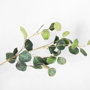May include: A sprig of artificial eucalyptus with green leaves. The leaves are oval shaped and have a slightly textured surface.