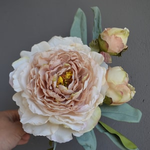 May include: A bouquet of artificial flowers featuring a large, pale pink peony and two smaller, cream-coloured peonies.