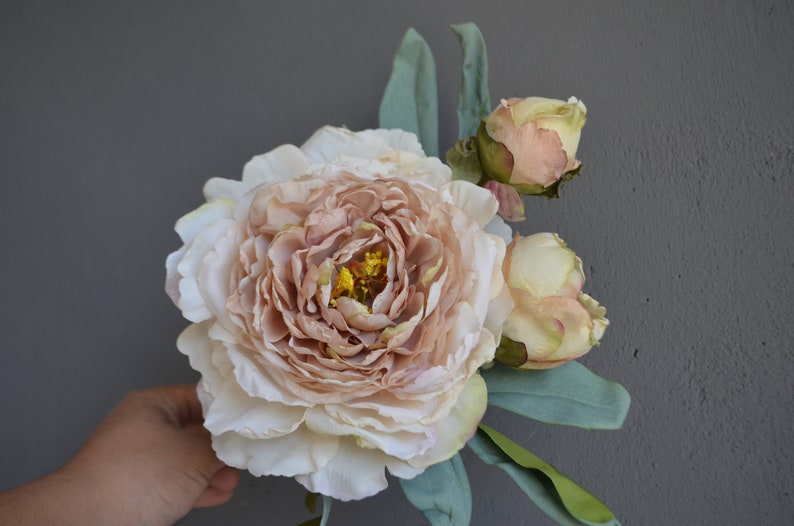 May include: A bouquet of artificial flowers featuring a large, pale pink peony and two smaller, cream-coloured peonies.