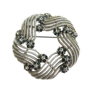 May include: A silver tone brooch with a woven design and blue and clear rhinestones.
