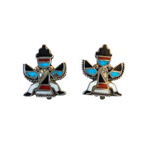 May include: A pair of silver earrings with a turquoise, red, black, and white inlay design. The earrings feature a stylized figure with wings.