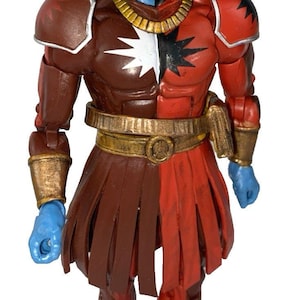 May include: Action figure of a character with a blue and black face, long black hair, and a red and brown costume. The figure has a gold-colored belt and wristbands. The character's chest is split, with a white star on one side and a black star on the other.