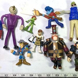 May include: A collection of colorful action figures, including Captain America with his shield, a figure in a purple suit, and other fantasy characters. The figures vary in size and design, showcasing a range of superhero and fantasy themes.
