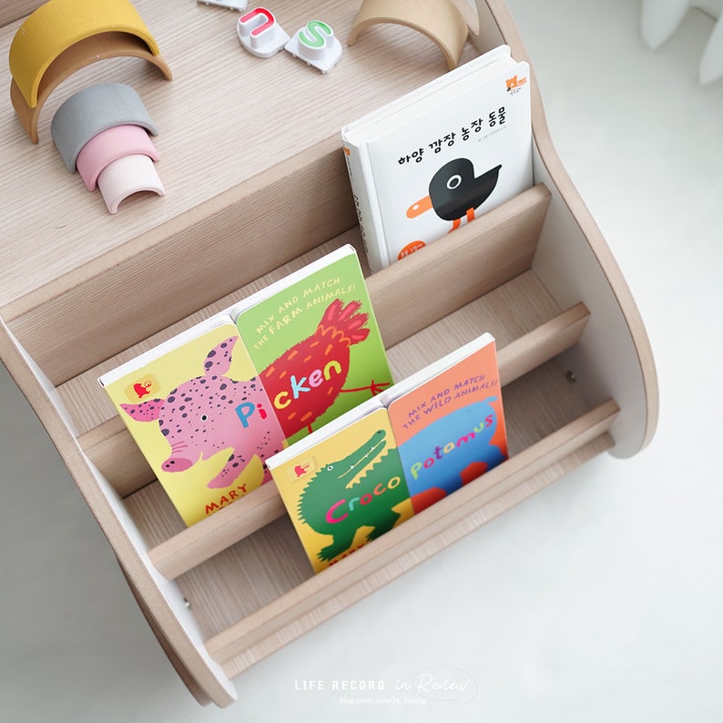 May include: A wooden bookshelf with rounded edges and shelves filled with colorful children's books. The books feature farm animals and wild animals with the text "Mix and Match the Farm Animals" and "Mix and Match the Wild Animals".