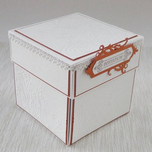 Könnte beinhalten: Weiße Pappbox mit dekorativem Spitzenbesatz und einem braunen Etikett mit der Aufschrift "Invitation".