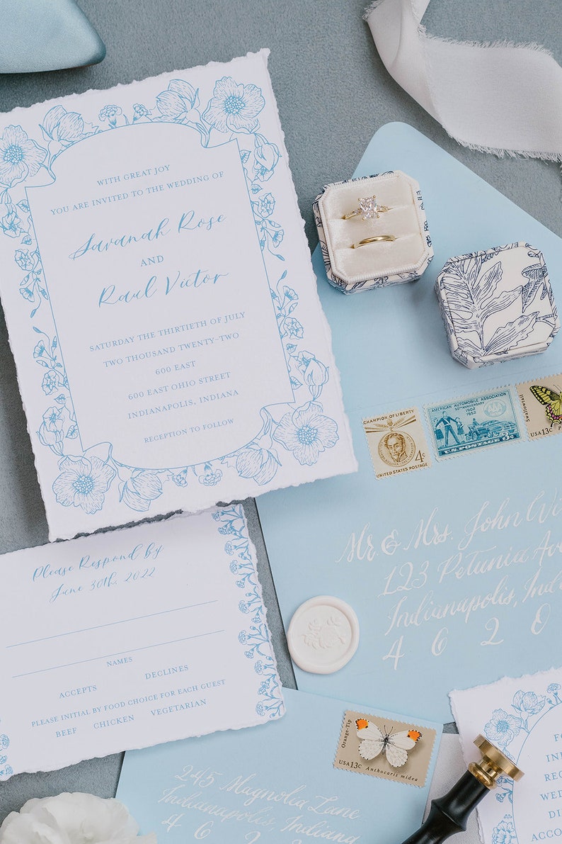 May include: A wedding invitation with a blue floral border and the text "With great joy you are invited to the wedding of Savanah Rose and Rael Victor" on a white background. The invitation includes the date, time, and location of the wedding. The invitation also includes a RSVP card with a blue floral border and the text "Please Respond by June 30th, 2022".