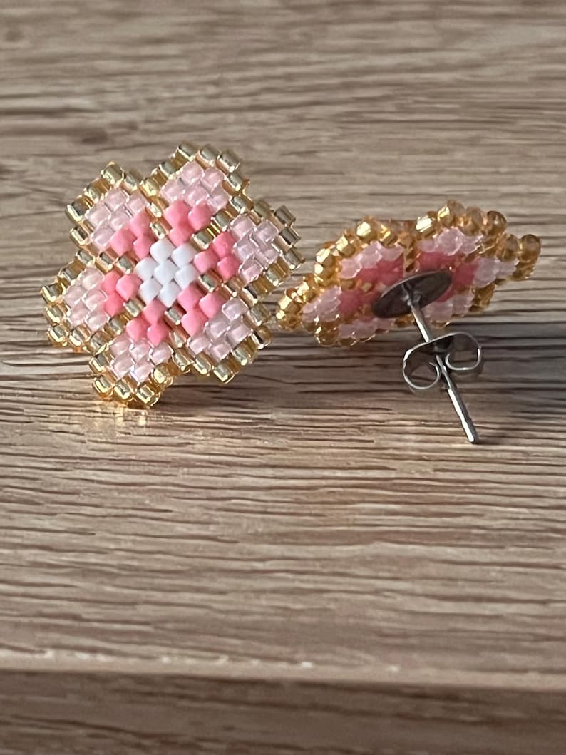 K&ouml;nnte beinhalten: Ein Paar rosa und goldene Ohrringe in Blumenform mit einem wei&szlig;en Zentrum. Die Ohrringe bestehen aus kleinen Perlen und haben einen Stiftverschluss.