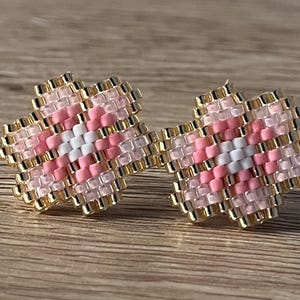 K&ouml;nnte beinhalten: Ein Paar rosa und wei&szlig;e, blumenf&ouml;rmige Ohrringe mit goldenen Akzenten. Die Ohrringe bestehen aus kleinen Perlen und sind so gestaltet, dass sie wie eine Blume aussehen.