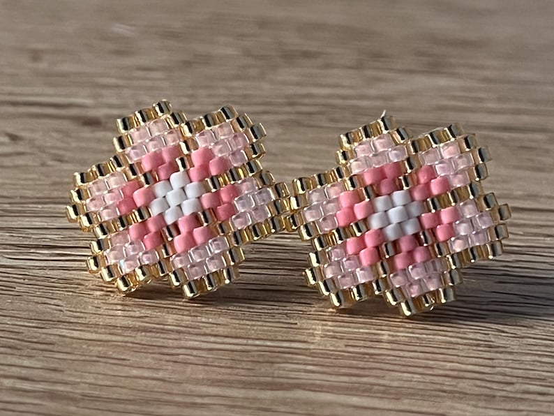 K&ouml;nnte beinhalten: Ein Paar rosa und wei&szlig;e, blumenf&ouml;rmige Ohrringe mit goldenen Akzenten. Die Ohrringe bestehen aus kleinen Perlen und sind so gestaltet, dass sie wie eine Blume aussehen.