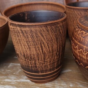 Op de afbeelding: Een verzameling handgemaakte bruine keramische potten. De set bevat een beker, kommen en een pot met deksel. Het aardewerk heeft een getextureerd oppervlak met donkerbruine accenten en een rustieke uitstraling. De stukken zijn op een houten oppervlak geplaatst.