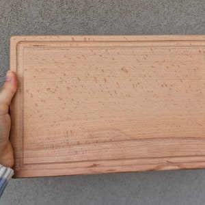 May include: A rectangular wooden cutting board with a light brown color and a slightly raised edge.