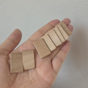 May include: A collection of eight small, rectangular, light-brown wooden tiles with a smooth, flat surface and visible natural wood grain patterns. The tiles are arranged in two separate groups, with two tiles in one group and six tiles in the other.