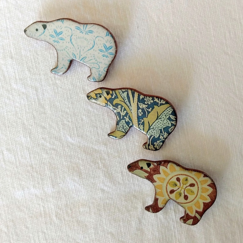 May include: Three ceramic polar bear pins with different patterned designs. The first pin is white with blue and light blue floral patterns. The second pin is blue with white and yellow floral patterns. The third pin is brown with yellow and orange floral patterns.