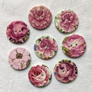 May include: A collection of seven circular buttons featuring various floral patterns in shades of pink, magenta, and green. Each button has two central holes for attachment and displays detailed illustrations of blooming roses and peonies.