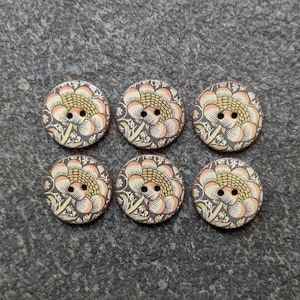 May include: Six round wooden buttons with a floral pattern. The buttons have a central flower with peach petals and a yellow centre, set against a dark grey background with green and cream leaves. Each button has two holes.