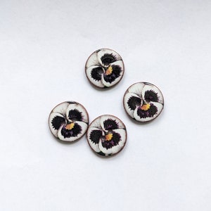 May include: Four round buttons featuring a detailed floral print of a pansy flower. Each button has a white background with deep purple, black, and yellow petal patterns. The buttons are circular with two small holes in the center for attachment.