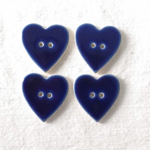 May include: Four navy blue heart-shaped buttons with two holes each. The buttons have a glossy finish and a white edge. These decorative buttons are perfect for sewing projects, adding a touch of charm to clothing or crafts.