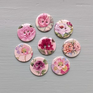Peut inclure: Un ensemble de sept boutons ronds, chacun arborant un motif floral unique. Les designs présentent diverses nuances de roses et de fleurs dans des tons rose, violet et pêche. Chaque bouton possède deux petits trous centraux pour la couture.