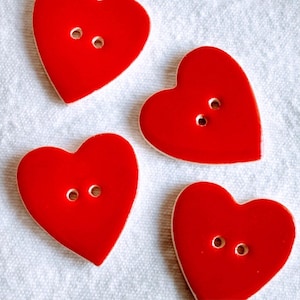 Può includere: Quattro bottoni rossi a forma di cuore con due fori ciascuno. I bottoni sono in ceramica e hanno una finitura lucida.