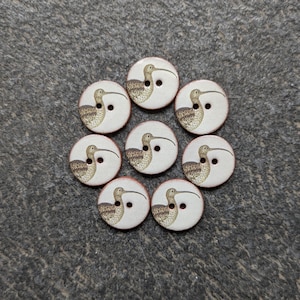 May include: Eight round buttons with a bird illustration. The buttons have a white background with a brown and tan bird design. Each button has two holes for sewing and a red edge.