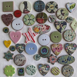 Puede incluir: Una colección de botones decorativos de varias formas y colores. Incluye botones redondos, de corazón, de estrella y cuadrados. Algunos presentan patrones florales, de pájaros y a cuadros. Otros son de colores lisos como rosa, amarillo y verde. Los botones tienen dos o cuatro agujeros.