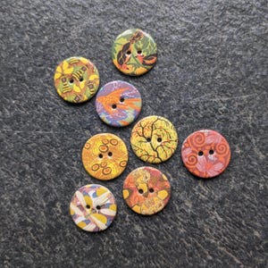 May include: Eight colourful round buttons with various nature-inspired designs, including birds, fish, bees, and floral patterns. The buttons are made of wood and have a glossy finish.