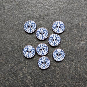 May include: Seven circular buttons featuring a white background with a repeating dark blue botanical pattern of branching stems and leaves. Each button is round and includes two small holes in the centre for attachment to fabric or garments.