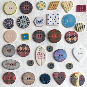 Peut inclure: Une collection de boutons assortis de formes, tailles et motifs variés, incluant des designs ronds, carrés, en forme de cœur et ovales. Les boutons présentent divers motifs tels que des carreaux, des fleurs, des papillons et des plumes.