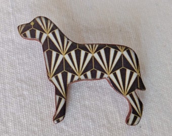 Puede incluir: Un pin en forma de perro blanco y negro con un patrón geométrico de abanicos dorados y blancos. El pin está hecho de madera y tiene un contorno marrón.
