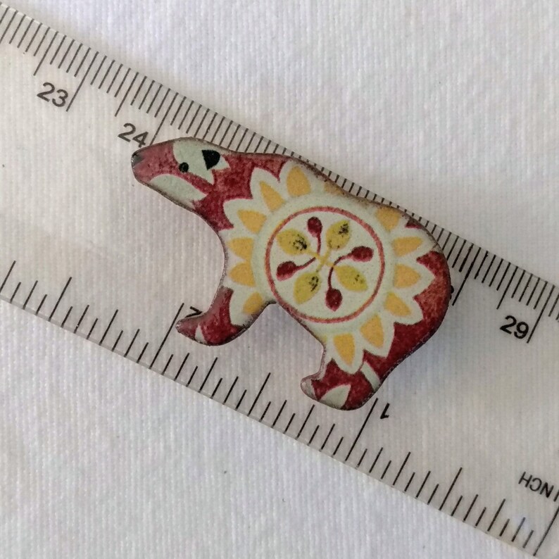 May include: A red, yellow, and white patterned ceramic bear figurine. The bear is standing on a white surface.