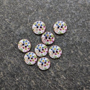 Puede incluir: Ocho botones redondos de madera con fondo blanco y un diseño floral en tonos azules, rosas y amarillos.