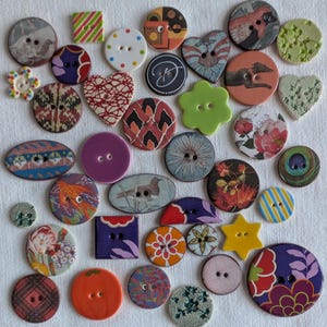 Puede incluir: Una colección de botones decorativos de diversas formas y colores. Los botones presentan diseños florales, geométricos y abstractos. Algunos tienen forma de corazón, cuadrado o estrella, con dos o cuatro agujeros para coser.