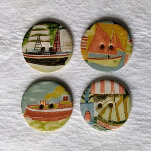 May include: Four circular buttons with maritime illustrations. Each button displays a different boat design in red, orange, blue, and green hues. The buttons have two sewing holes and are set against a white backdrop.