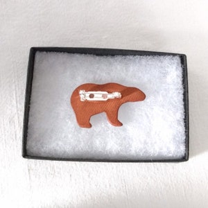May include: A brown ceramic bear pin with a silver pin back. The bear is in a white box with a brown lining.