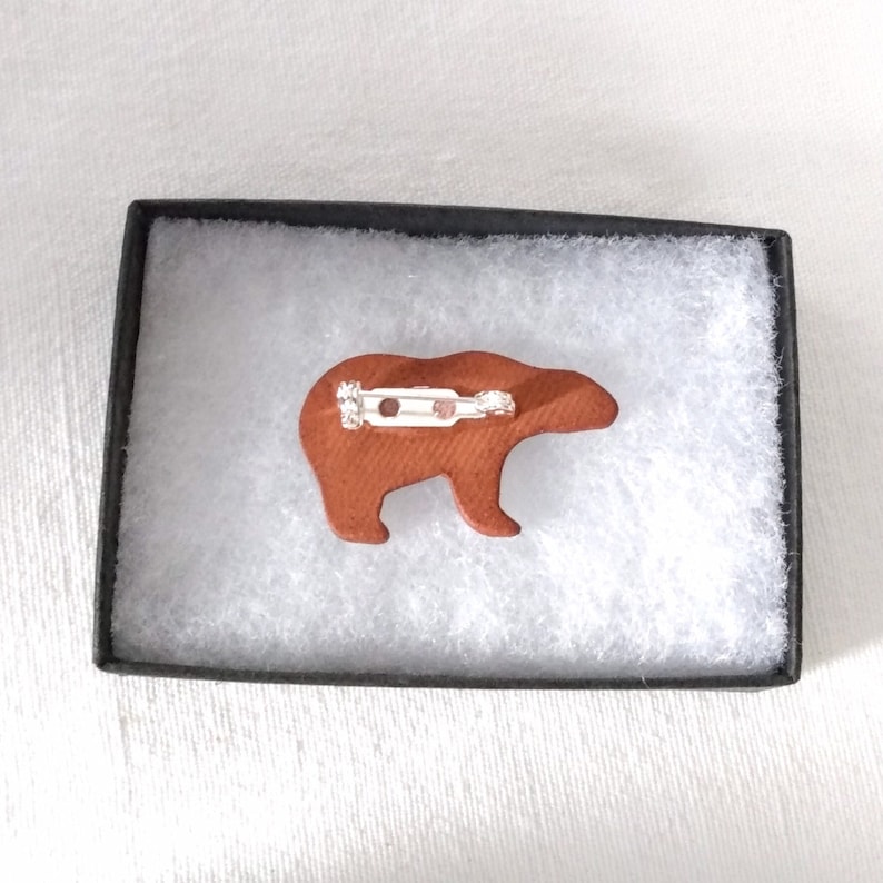 May include: A brown ceramic bear pin with a silver pin back. The bear is in a white box with a brown lining.