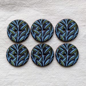 May include: Six round buttons with a botanical design. The buttons feature a dark blue background with a pattern of blue and green leaves. Each button has two holes for sewing and a dark brown edge.
