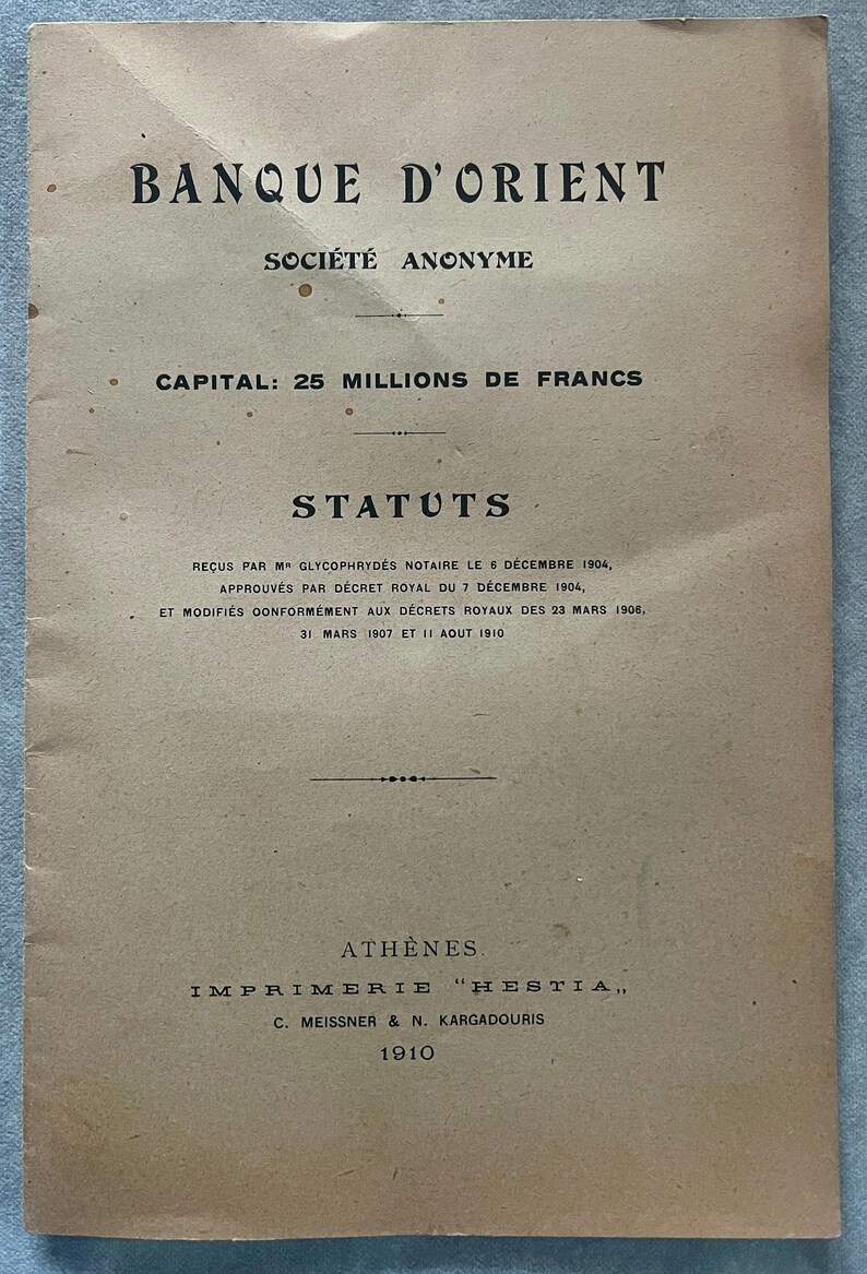 May include: A vintage document with the title "BANQUE D'ORIENT" and the text "SOCI&Eacute;T&Eacute; ANONYME" in black ink. The document is printed on aged, tan paper and includes the text "CAPITAL: 25 MILLIONS DE FRANCS" and "STATUTS". The document is dated 1910.
