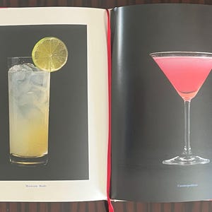 May include: Two cocktails, one with a lime wedge and the other a pink cocktail in a martini glass. The cocktails are on a black background with the names "Moscow Mule" and "Cosmopolitan" printed below each.