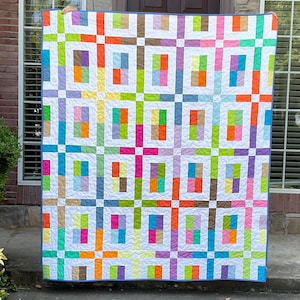 May include: A rectangular quilt featuring a grid pattern of white fabric strips separating small, multi-colored rectangular blocks. The blocks display a variety of colors including orange, green, blue, pink, purple, and brown, all finished with a blue border.