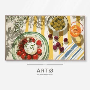 May include: A framed painting depicts a still life with food and drink. A plate of tomatoes and cheese, a bowl of olives, cherries, and a glass of orange liquid are arranged on a yellow and white striped tablecloth. The painting includes the text "ARTØ VINTAGE FRAME TV ART."